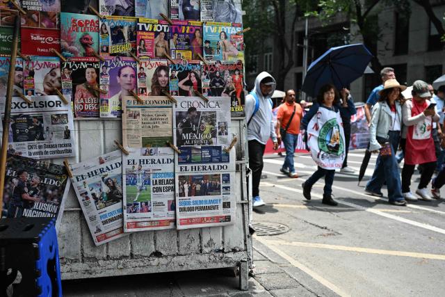Teachers from the National Coordinator of Education Workers (CNTE), who have been protesting for weeks demanding salary increases and opposing the FIFA World Cup, march past a newsstand displaying front pages highlighting the Mexican national team’s victory as they head towards the Ministry of the Interior in Mexico City on June 19, 2026. (Photo by Yuri CORTEZ / AFP)