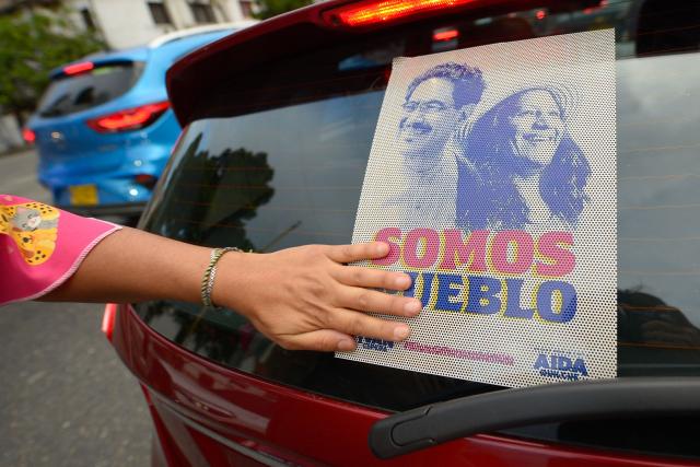 A supporter of Colombia's presidential candidate Ivan Cepeda sticks a campaign poster bearing his image alongside running mate Aida Quilcue, reading "Somos Pueblo" (We are the people), onto a vehicle in Bogota on June 19, 2026. Colombians vote on June 21, 2026 in a presidential runoff pitting a hard-right opera-singer-turned-lawyer against a leftist senator, an election with stark consequences for the country's stumbling peace process with armed groups and strained ties with Washington. (Photo by Sebastian BARROS / AFP)