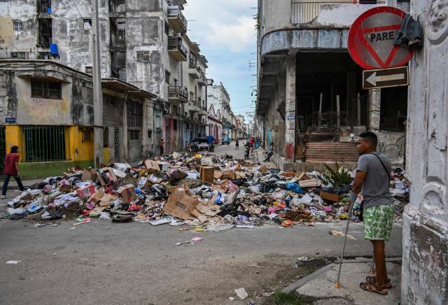 People walk past garbage dumped on a street in Havana, on June 19, 2026. (Photo by YAMIL LAGE / AFP)