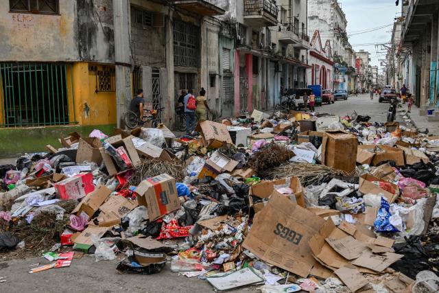 People walk past garbage dumped on a street in Havana, on June 19, 2026. (Photo by YAMIL LAGE / AFP)