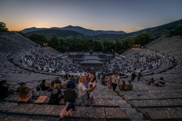 Spectators take a selfie before the start of the opera 'Medea' at the Ancient Greek theatre of former city Epidaurus, in Nea Epidavros on June 18, 2026. With flamboyant costumes reminiscent of those from 1961, and a production reconstructed using notebooks and photographs from the period: 'Medea', the opera that brought Maria Callas her triumph, is being revived at the ancient Greek theatre of Epidaurus. During a one-off, sold-out performance on Saturday evening, the Greek National Opera returns for the first time in 65 years to this 4th-century BC amphitheatre, 200 kilometres from Athens, renowned for its exceptional acoustics. (Photo by Aris MESSINIS / AFP)