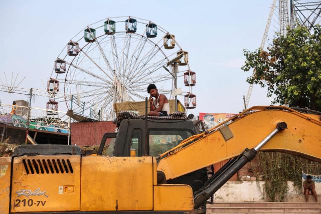 A construction worker speaks on a mobile phone as he rests atop a JCB at Assi Ghat along the banks of the river Ganges in Varanasi on June 20, 2026. (Photo by Niharika KULKARNI / AFP)