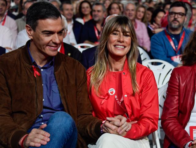 (FILES) Spain's prime minister Pedro Sanchez (L) holds hands with his wife Begona Gomez at the start of the 41st congress of the Spanish Socialist Workers Party (PSOE) at the Palacio de Exposiciones in Seville, on December 1, 2024. A Spanish court has ordered the wife of Prime Minister Pedro Sanchez, Begona Gomez, to stand trial for corruption and banned her from leaving the country, according to a court order released on June 20, 2026. Judge Juan Carlos Peinado ordered Gomez to hand in her passport and to check in with the authorities twice a month until a verdict is reached in the case, the ruling said. (Photo by CRISTINA QUICLER / AFP)