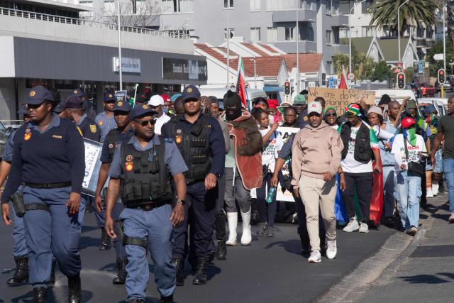 South African Police officers lead a group of about 100 people, some carrying banners and waving South African flags, taking part in a march, organised by the March and March movement, protesting against illegal immigrants, in Wynberg, a Cape Town suburb, on June 20, 2026. (Photo by RODGER BOSCH / AFP)