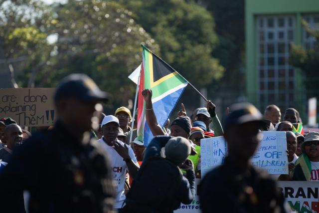 South African Police officers keep an eye on a  group of about 100 people, some carrying banners and waving South African flags, taking part in a march, organised by the March and March movement, protesting against illegal immigrants, in Wynberg, a Cape Town suburb, on June 20, 2026. (Photo by RODGER BOSCH / AFP)