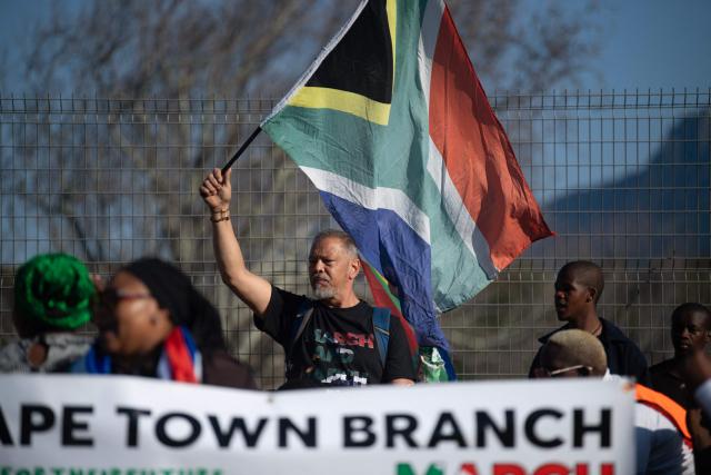A group of about 100 people, some carrying banners and waving South African flags, take part in a march, organised by the March and March movement, protesting against illegal immigrants, in Wynberg, a Cape Town suburb, on June 20, 2026. (Photo by RODGER BOSCH / AFP)