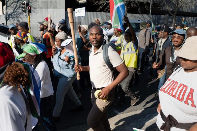 A man carrying a baton joins a group of about 100 people, some carrying banners and waving South African flags, taking part in a march, organised by the March and March movement, protesting against illegal immigrants, in Wynberg, a Cape Town suburb, on June 20, 2026. (Photo by RODGER BOSCH / AFP)
