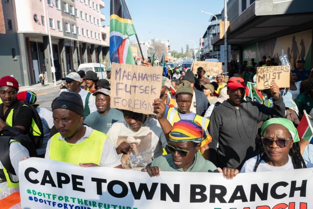 A group of about 100 people, some carrying banners and waving South African flags, take part in a march, organised by the March and March movement, protesting against illegal immigrants, in Wynberg, a Cape Town suburb, on June 20, 2026. (Photo by RODGER BOSCH / AFP)