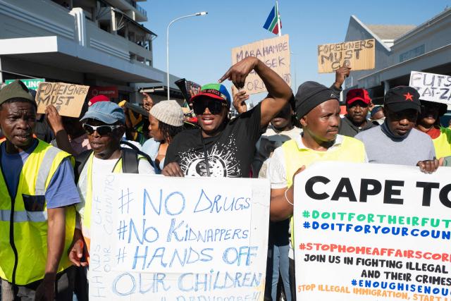 A group of about 100 people, some carrying banners and waving South African flags, take part in a march, organised by the March and March movement, protesting against illegal immigrants, in Wynberg, a Cape Town suburb, on June 20, 2026. (Photo by RODGER BOSCH / AFP)