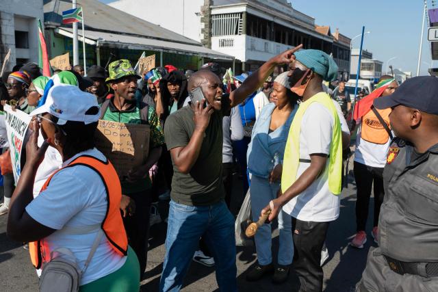 Marchers gesture towards people(not visible) they think are foreigners, as a group of about 100 people, some carrying banners and waving South African flags, take part in a march, organized by March and March, protesting against illegal immigrants, in Wynberg, a Cape Town suburb, on June 20, 2026. (Photo by RODGER BOSCH / AFP)