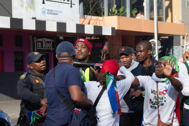 Marshalls intervene as a marcher (red cap) threatens a journalist (blue cap), as a group of about 100 people, take part in a march, organised by the March and March movement, protesting against illegal immigrants, in Wynberg, a Cape Town suburb, on June 20, 2026. (Photo by RODGER BOSCH / AFP)