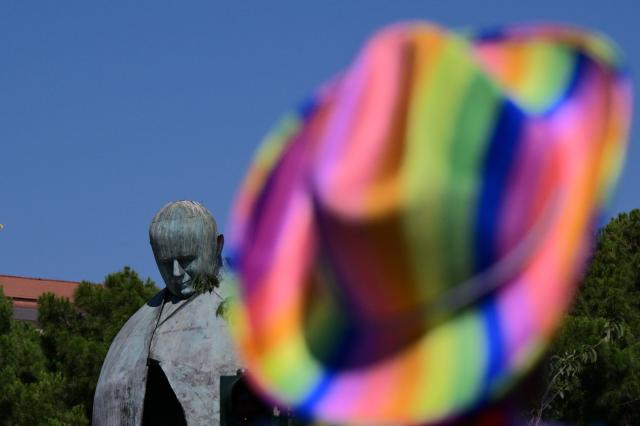 A person wearing a rainbow hat walks past a statue of Pope John Paul II during the Pride March in Rome on June 20, 2026. (Photo by Tiziana FABI / AFP)