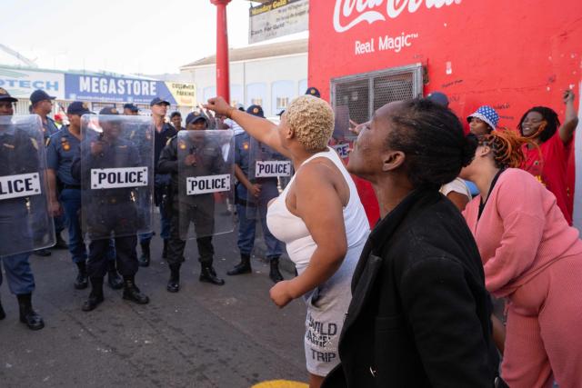A group of people against the a foreigners are separated by a line of South African Police officers with riot shields, from about 100 people (not visible), taking part in a march, organised by the March and March movement, protesting against illegal immigrants, in Wynberg, a Cape Town suburb, on June 20, 2026. (Photo by RODGER BOSCH / AFP)
