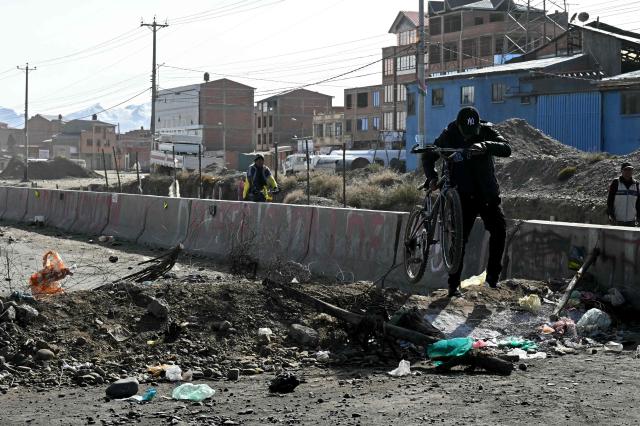 A man lifts a bicycle to go through a barricade at a blockade zone in Cruce Ventilla in El Alto, Bolivia on June 20, 2026, after Bolivian President Rodrigo Paz declared state of emergency. Bolivian President Rodrigo Paz declared a state of emergency across the Latin American country after more than six weeks of road blockades and protests demanding his resignation, saying he had exhausted "all avenues of dialogue." (Photo by AIZAR RALDES / AFP)