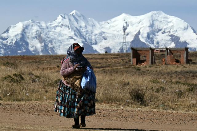 A local walks with the Huayna Potosi mountain in the background, while eluding a blockade in Mazo Cruz, La Paz department, Bolivia on June 20, 2026, after Bolivian President Rodrigo Paz declared state of emergency. Bolivia's president declared a state of emergency and deployed police and bulldozers to clear anti-government roadblocks that have paralyzed the Andean nation for more than six weeks. An array of anti-government unions, Indigenous groups and coca farmers have marched through cities and blocked main roads across the country with rubble, logs and debris. (Photo by AIZAR RALDES / AFP)