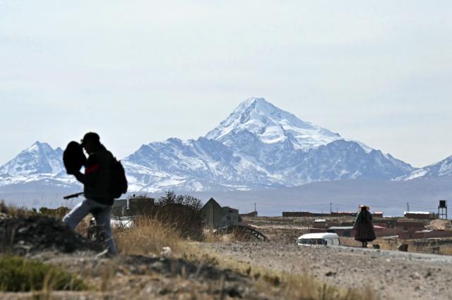 Locals walk with the Huayna Potosi mountain in the background in Mazo Cruz, La Paz department, Bolivia on June 20, 2026, after Bolivian President Rodrigo Paz declared state of emergency. Bolivia's president declared a state of emergency and deployed police and bulldozers to clear anti-government roadblocks that have paralyzed the Andean nation for more than six weeks. An array of anti-government unions, Indigenous groups and coca farmers have marched through cities and blocked main roads across the country with rubble, logs and debris. (Photo by AIZAR RALDES / AFP)