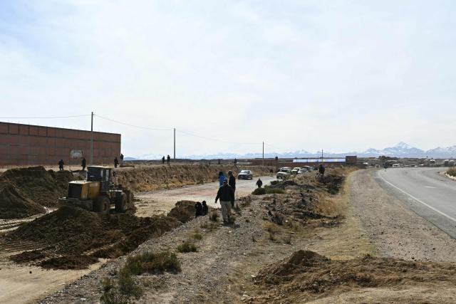 A woman walks in the highway as a backhoe bucket clears the roadblock in Mazo Cruz, La Paz department, Bolivia on June 20, 2026, after Bolivian President Rodrigo Paz declared state of emergency. Bolivia's president declared a state of emergency and deployed police and bulldozers to clear anti-government roadblocks that have paralyzed the Andean nation for more than six weeks. An array of anti-government unions, Indigenous groups and coca farmers have marched through cities and blocked main roads across the country with rubble, logs and debris. (Photo by AIZAR RALDES / AFP)