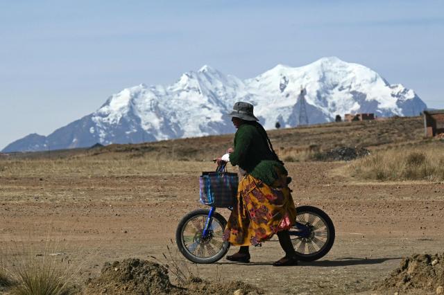 A local walks with a bike with the Huayna Potosi mountain in the background, while eluding a blockade in Mazo Cruz, La Paz department, Bolivia on June 20, 2026, after Bolivian President Rodrigo Paz declared state of emergency. Bolivia's president declared a state of emergency and deployed police and bulldozers to clear anti-government roadblocks that have paralyzed the Andean nation for more than six weeks. An array of anti-government unions, Indigenous groups and coca farmers have marched through cities and blocked main roads across the country with rubble, logs and debris. (Photo by AIZAR RALDES / AFP)