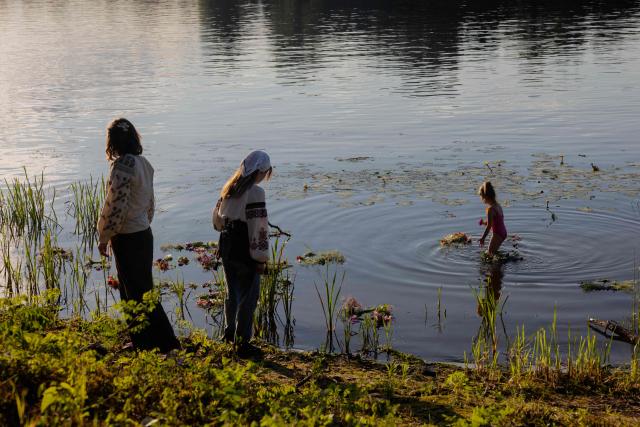 Young girls look on as flower wreaths float on the water during a picnic in the spirit of the Ivan Kupala holiday organized by the Veterans Corps for soldiers, veterans, and their families in Kyiv on June 20, 2026, amid the Russian invasion of Ukraine. (Photo by Tetiana DZHAFAROVA / AFP)