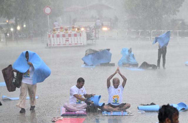 Unwavering yoga enthousiasts brave the pouring rain as they take part in the international yoga day, on June 21, 2026 in Berlin, Germany. (Photo by RALF HIRSCHBERGER / AFP)