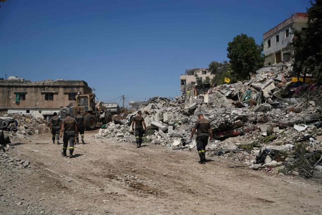 Lebanese civil defence workers walk behind a bulldozer as it removes the rubble from the main market place destroyed by the Israeli military in the southern city of Nabatieh on June 21, 2026. The first round of negotiations between the United States and Iran since the two sides signed a preliminary agreement to halt their war was due to begin in Switzerland on June 21, with the conflict in Lebanon threatening the deal. Lebanon was drawn into the Middle East war on March 2 when Tehran-backed militant group Hezbollah launched attacks on Israel to avenge the killing of the Iranian leader. Israel has responded with broad strikes across Lebanon and a ground offensive. (Photo by Abbas FAKIH / AFP) / 