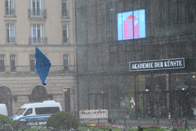 A yoga mat (L) is swept across the square by the wind through the pouring rain during an event to mark the international yoga day, on June 21, 2026 in Berlin, Germany. (Photo by RALF HIRSCHBERGER / AFP)
