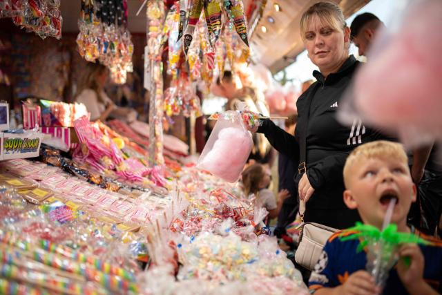 Members of the public buy sweets from a stall as they attend The Hoppings fun fair, believed to be one of the largest travelling funfairs in Europe, in Newcastle upon Tyne, north east England on June 20, 2026. The fun fair, which originally began as a Temperance Fair in 1882, comprises of over 400 attractions set up on the city's Town Moor. The fair runs until June 28, 2026 and is expected to attract around 500,000 people. (Photo by Oli SCARFF / AFP)