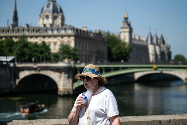 A woman with a hat cools off with a cold bottle of water on the Seine riverside with the Paris commercial court (L) and the Conciergerie buildings and the Pont Notre Dame in the background as France experiences a heat wave in Paris, France, on June 21, 2026. The climb of the thermometer continues in France as Météo-France has placed 35 départements on red heatwave alert for June 21, 2026, a record figure that includes 26 million French people, already knocked out on June 20 by the stifling heat. (Photo by ARNAUD FINISTRE / AFP)