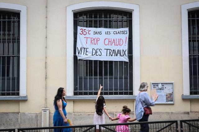 (FILES) A young girl points at a banner which reads "35 degrees in the classrooms, too hot. Work needs to be done quickly" as she walks past a school in Paris on June 18, 2026. A total of 845 primary and secondary schools will be closed on June 21, 2026 in France due to the heatwave, whilst a further 1,800 schools will "adjust their timetables", meaning they will "dismiss pupils in the early afternoon", France's Education Minister announced on June 21, 2026. (Photo by Simon WOHLFAHRT / AFP)
