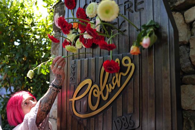 An attendee places a flower on a memorial during a "Run Coluche" biker gathering as part of a tribute to French comedian and actor Coluche 40 years after his death, in Opio, southeastern France, on June 21, 2026. (Photo by Valery HACHE / AFP)