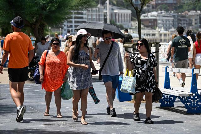 People walk on the esplanade along La Concha bay beach in the Spanish Basque city of San Sebastian, on June 21, 2026, first day of the first official heatwave of this summer. Spain's first official heatwave of this summer begins today and will last until at least June 24, 2026. The State Meteorological Agency (Aemet), the body responsible for declaring these types of episodes when they meet specific criteria regarding intensity, duration, and territorial extension, activated a special weather warning two days ago. (Photo by ANDER GILLENEA / AFP)