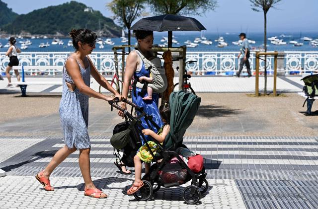 People walk on the esplanade along La Concha bay beach in the Spanish Basque city of San Sebastian, on June 21, 2026, first day of the first official heatwave of this summer. Spain's first official heatwave of this summer begins today and will last until at least June 24, 2026. The State Meteorological Agency (Aemet), the body responsible for declaring these types of episodes when they meet specific criteria regarding intensity, duration, and territorial extension, activated a special weather warning two days ago. (Photo by ANDER GILLENEA / AFP)