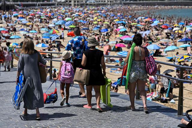 People walk on the esplanade along La Concha bay beach in the Spanish Basque city of San Sebastian, on June 21, 2026, first day of the first official heatwave of this summer. Spain's first official heatwave of this summer begins today and will last until at least June 24, 2026. The State Meteorological Agency (Aemet), the body responsible for declaring these types of episodes when they meet specific criteria regarding intensity, duration, and territorial extension, activated a special weather warning two days ago. (Photo by ANDER GILLENEA / AFP)