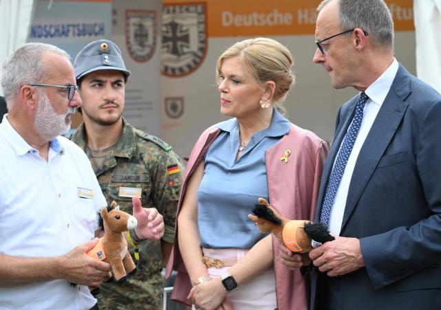 German Chancellor Friedrich Merz (R) holds a soft toy mule as he stands next to the President of the Bundestag (lower house of parliament) Julia Kloeckner (2nd R) and speaks with representatives of the mountain rangers of the German armed forces (Bundeswehr) during an event to mark the National Veterans' Day on June 21, 2026 in Berlin. The achievements of serving and former soldiers of the German armed forces (Bundeswehr) is honoured through events held across the country and a central celebration in Berlin. (Photo by RALF HIRSCHBERGER / AFP)
