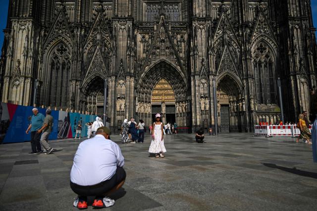 A man takes a photo of a girl in front of the Cologne cathedral, western Germany on June 21, 2026. From July 1, 2026 tourists will only be able to enter the interior of Cologne Cathedral after purchasing a ticket. Attendance at church services will remain free of charge without restriction. (Photo by Ina FASSBENDER / AFP)