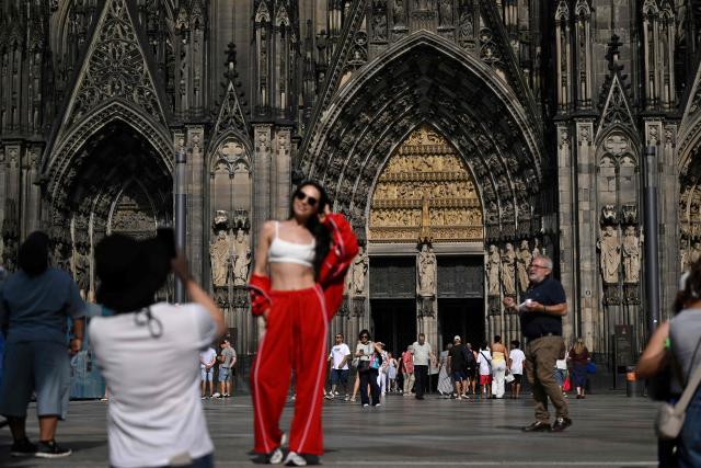 A woman poses in front of the Cologne cathedral, western Germany on June 21, 2026. From July 1, 2026 tourists will only be able to enter the interior of Cologne Cathedral after purchasing a ticket. Attendance at church services will remain free of charge without restriction. (Photo by Ina FASSBENDER / AFP)