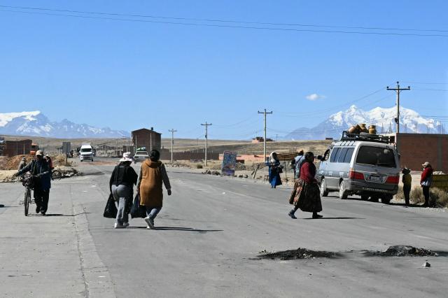 Locals cross the road linking Desaguaderos-La Paz, in Laja, Bolivia, on June 21, 2026, a day after Bolivia's President Rodrigo Paz declared a state of emergency. Bolivian police driving bulldozers cleared highways and fuel trucks rolled into La Paz after the president declared a state of emergency to remove anti-government roadblocks promoted by unions, Indigenous groups, and coca growers that had paralyzed the Andean nation for more than six weeks. (Photo by AIZAR RALDES / AFP)