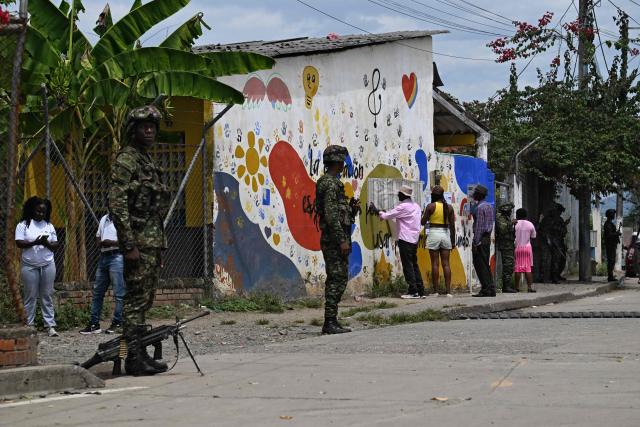 People look at an electoral roll outside a polling center near soldiers during the presidential election runoff, in Villa Paz, Valle del Cauca, Colombia, on June 21, 2026. Colombians head to the polls to pick a new president between a hard-right White House-backed lawyer and a leftist senator that will decide the fate of the country's stumbling peace process and strained ties with Washington. (Photo by Joaquin SARMIENTO / AFP)