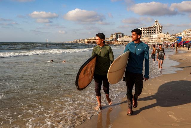 Youths walk with surfboards along a beach by the Mediterranean sea in Gaza City on June 21, 2026. The ceasefire between Israel and the Palestinian Islamist movement Hamas came into effect in Gaza in October 2025 after two years of devastating war. But the tiny coastal territory remains gripped by bloodshed, with each side accusing the other of near-daily violations. (Photo by Omar AL-QATTAA / AFP)