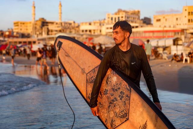 Palestinian surfer Hussein Abu Assi, 23, takes his surfboard out into the Mediterranean sea off a beach in Gaza City on June 21, 2026. The ceasefire between Israel and the Palestinian Islamist movement Hamas came into effect in Gaza in October 2025 after two years of devastating war. But the tiny coastal territory remains gripped by bloodshed, with each side accusing the other of near-daily violations. (Photo by Omar AL-QATTAA / AFP)