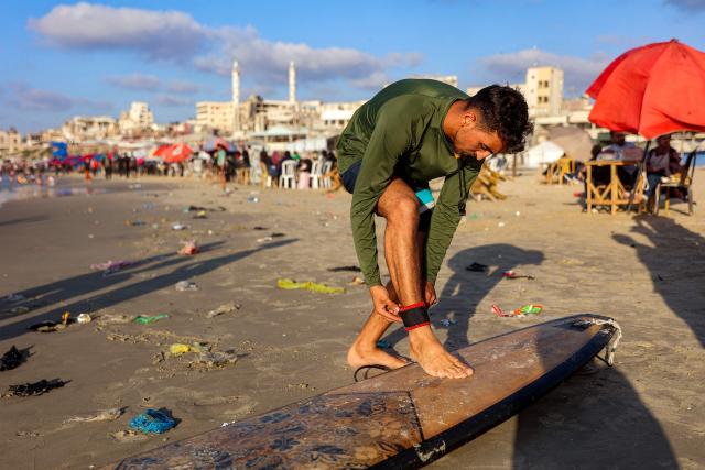 Palestinian surfer Hussein Abu Assi, 23, adjusts the leash on his surfboard at a beach along the Mediterranean sea in Gaza City on June 21, 2026. The ceasefire between Israel and the Palestinian Islamist movement Hamas came into effect in Gaza in October 2025 after two years of devastating war. But the tiny coastal territory remains gripped by bloodshed, with each side accusing the other of near-daily violations. (Photo by Omar AL-QATTAA / AFP)