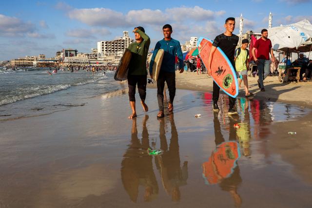 Youths walk with surfboards along a beach by the Mediterranean sea in Gaza City on June 21, 2026. The ceasefire between Israel and the Palestinian Islamist movement Hamas came into effect in Gaza in October 2025 after two years of devastating war. But the tiny coastal territory remains gripped by bloodshed, with each side accusing the other of near-daily violations. (Photo by Omar AL-QATTAA / AFP)