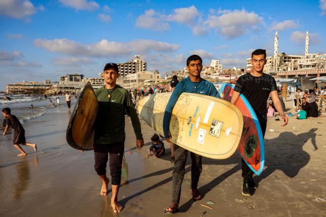 Youths walk with surfboards along a beach by the Mediterranean sea in Gaza City on June 21, 2026. The ceasefire between Israel and the Palestinian Islamist movement Hamas came into effect in Gaza in October 2025 after two years of devastating war. But the tiny coastal territory remains gripped by bloodshed, with each side accusing the other of near-daily violations. (Photo by Omar AL-QATTAA / AFP)