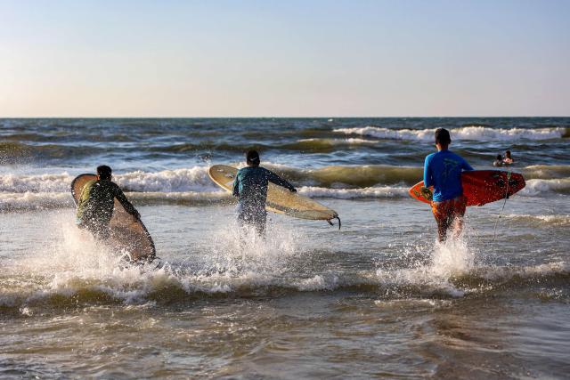 Youths take their surfboards out into the Mediterranean sea off a beach in Gaza City on June 21, 2026. The ceasefire between Israel and the Palestinian Islamist movement Hamas came into effect in Gaza in October 2025 after two years of devastating war. But the tiny coastal territory remains gripped by bloodshed, with each side accusing the other of near-daily violations. (Photo by Omar AL-QATTAA / AFP)