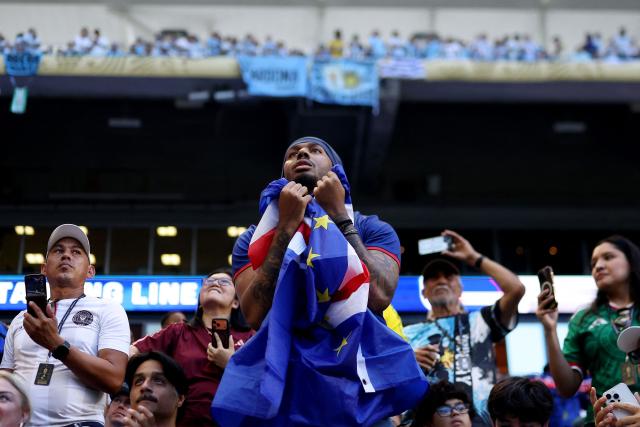 A Cape Verde fan gestures as he holds a national flag during the 2026 World Cup Group H football match between Uruguay and Cape Verde at the Miami Stadium in Miami Gardens on June 21, 2026.  (Photo by PATRICIA DE MELO MOREIRA / AFP)