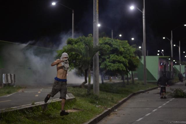 A demonstrator runs from tear gas as they protest against the preliminary results of the presidential runoff election in Cali, Colombia, on June 21, 2026. A flamboyant US-backed lawyer who has never held public office narrowly won Colombia's presidential runoff Sunday, swinging the country hard to the right on a promise to wage war against drug-running guerrilla groups. With more than 99 percent of polling centers reporting, Abelardo de la Espriella had 49.67 percent of the vote, an unassailable lead over his rival, left-wing Senator Ivan Cepeda who trailed at 48.69 percent, according to official results. (Photo by JOAQUIN SARMIENTO / AFP)
