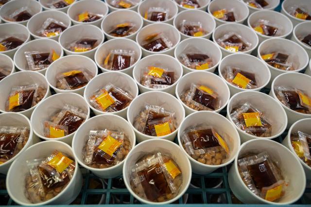 This photo taken on May 15, 2026 shows cups of natto awaiting to be sealed at the Kamakurayama Natto production facility in Kamakura, Kanagawa prefecture. The highly nutritious beans inoculated with beneficial bacteria remain a traditional Japanese breakfast staple, but their pungent aroma, viscous texture and yeasty taste divide even their homeland. Recent years have seen natto join a series of fermented foods, from kimchi to kombucha, that have surged in popularity worldwide as Americans in particular seek better digestive health following the Covid-19 pandemic. (Photo by Andrew CABALLERO-REYNOLDS / AFP) / To go with AFP story Japan-food-health-natto-lifestyle,FEATURE by Tomohiro Osaki and Sarah Lai