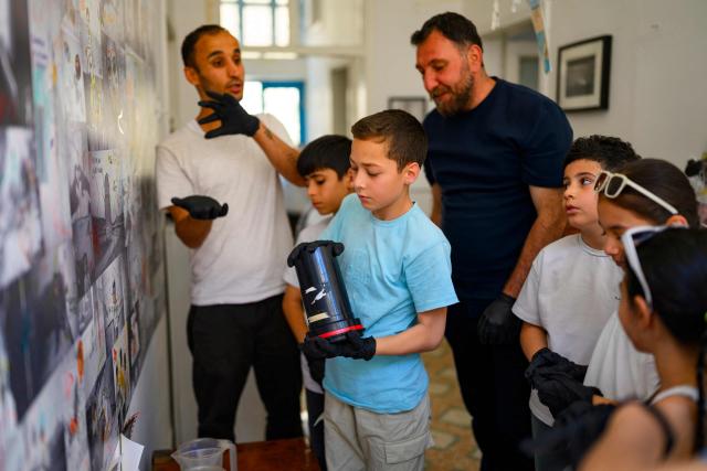 Children develop camera films with their educators and the project's co-founders, photographers Serbest Salih (L) and Amar Kilic (3rd R) during a workshop held as part of Fotohane Darkroom project in Mardin, southeastern Turkey, on June 13, 2026. In a dimly lit room illuminated by a pair of red lamps, eight-year-old Zeynep waits to see the photographs she has taken, now trapped as shadows and silhouettes on a roll of film. Originally from the southeastern province of Mardin, Zeynep is among eight children taking part in a two-month analog photography workshop for local and migrant youth near Turkey's borders with Iraq and Syria. The project, called Fotohane Darkroom, started in Mardin in 2024, by Kilic and Syrian photographer and educator Serbest Salih. In Turkish, Arabic, Kurdish and Persian, Fotohane means "house of photo", a name chosen by the children. (Photo by Yasin AKGUL / AFP)