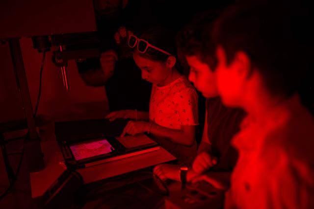 Children work in a darkroom during a workshop held as part of Fotohane Darkroom project in Mardin, southeastern Turkey, on June 14, 2026. In a dimly lit room illuminated by a pair of red lamps, eight-year-old Zeynep waits to see the photographs she has taken, now trapped as shadows and silhouettes on a roll of film. Originally from the southeastern province of Mardin, Zeynep is among eight children taking part in a two-month analog photography workshop for local and migrant youth near Turkey's borders with Iraq and Syria. The project, called Fotohane Darkroom, started in Mardin in 2024, by Kilic and Syrian photographer and educator Serbest Salih. In Turkish, Arabic, Kurdish and Persian, Fotohane means "house of photo", a name chosen by the children. (Photo by Yasin AKGUL / AFP)