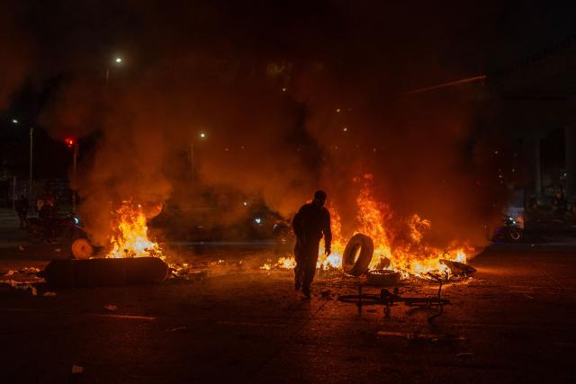 TOPSHOT - A man throws a tire into a fire during clashes with police as demonstrators protest against the preliminary results of the presidential runoff election in Bogotá, Colombia, on June 21, 2026. A flamboyant US-backed lawyer who has never held public office narrowly won Colombia's presidential runoff Sunday, swinging the country hard to the right on a promise to wage war against drug-running guerrilla groups. With more than 99 percent of polling centers reporting, Abelardo de la Espriella had 49.67 percent of the vote, an unassailable lead over his rival, left-wing Senator Ivan Cepeda who trailed at 48.69 percent, according to official results. (Photo by Diego Cuevas / AFP)
